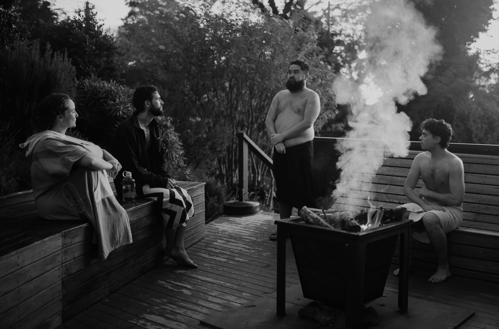 Four people around a fire pit on a deck outside the sauna at dusk